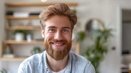 A young man is smiling for the camera. He has a beard and his hair is light brown in color. He's dressed casually with a denim shirt.