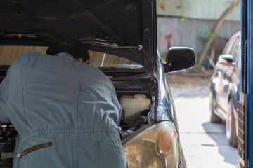 A professional auto mechanic in blue coveralls checking the engine under the open hood at a service station for vehicle maintenance and safety.