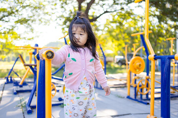 A cute little Asian girl is playing on the playground equipment at Sa Kaeo,asian girl playing in playground,Young girl sitting on yellow playground equipment