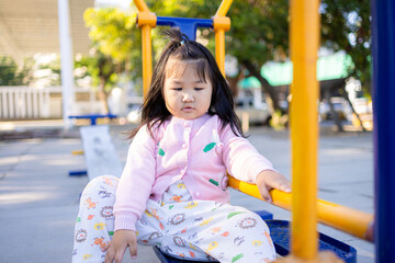 A cute little Asian girl is playing on the playground equipment at Sa Kaeo,asian girl playing in playground,Young girl sitting on yellow playground equipment