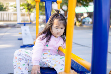 A cute little Asian girl is playing on the playground equipment at Sa Kaeo,asian girl playing in playground,Young girl sitting on yellow playground equipment