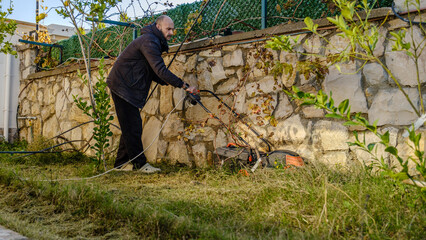 A middle-aged man mowing the grass in his garden with a lawnmower on a winter day