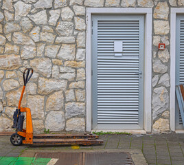 Manual Forklift Pallet Jack in Front of Metal Door Stone Wall Storage Building