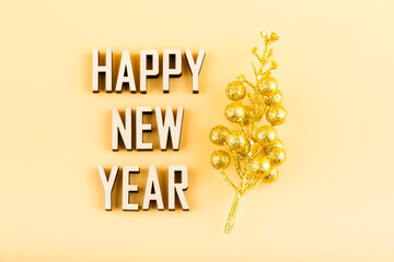 Text Happy New Year made of wooden letters on a yellow background next to a golden branch. Christmas greeting card.