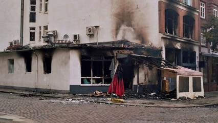 Photograph of a fire-damaged urban building with blackened windows, smoke stains, and visible destruction at street level.