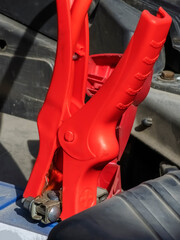 Close-up of a car charger cable jump starting a dead car battery. Red charging cable clamps on battery terminals for charging, car repair and maintenance concept.