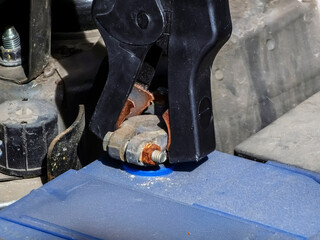 Close-up of car charger cable jump starting dead car battery. Black charging cable clamps on battery terminals for charging, car repair and maintenance concept.