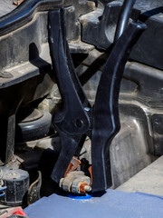 Close-up of car charger cable jump starting a dead car battery. Black charging cable clamps on battery terminals for charging, car repair and maintenance concept.