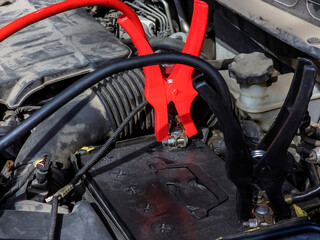 Close-up of car charger cable jump starting a dead car battery. Black and red charging cable clamps on a battery terminals for charging, car repair and maintenance concept.
