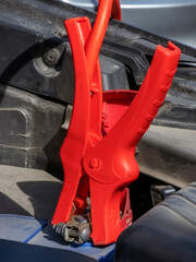 Close-up of car charger cable jump starting dead car battery. Red charging cable clamps on battery terminals for charging, car repair and maintenance concept.