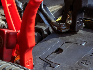 Close-up of car charger cable jump starting a dead car battery. Red charging cable clamps on battery terminals for charging, car repair and the maintenance concept.