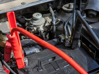 Close-up of car charger cable jump starting dead car battery. Black and red charging cable clamps on battery terminals for charging, car repair and maintenance concept.