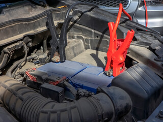 Close-up of car charger cable jump starting a dead car battery. Black and red charging cable clamps on battery terminals for charging, car repair and maintenance concept.