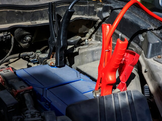 Close-up of the car charger cable jump starting a dead car battery. Black and red charging cable clamps on battery terminals for charging, car repair and maintenance concept.
