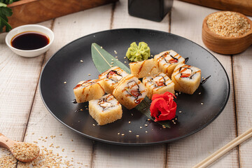 Crispy tempura sushi rolls topped with sauce and sesame seeds served on a black plate with ginger and wasabi © Hihitetlin