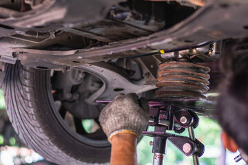 Close-up of a mechanic's gloved hand using a jack to support engine or suspension components while working underneath a car in a garage.
