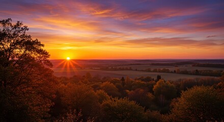 Radiant sun descends over rolling hills and dense forest canopy at dusk