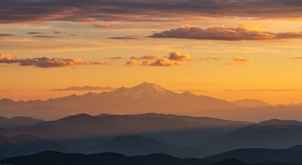 Distant snowcapped mountain peak rises above layered ridges during vibrant sunset
