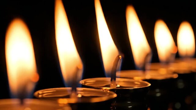 row of burning oil lamps with bright flickering flames on dark background