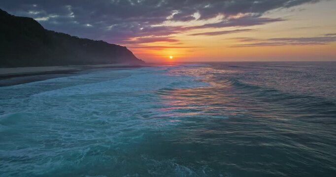Indonesia, Bali: amazing beautiful sunset over ocean, painting sky with warm colors and reflecting on the turquoise waves breaking along the tropical coastline. Natural background. Aerial drone flight