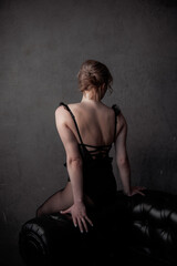 Rear view of a woman in a black bodysuit sitting on a classic leather Chesterfield sofa against a textured grey wall.