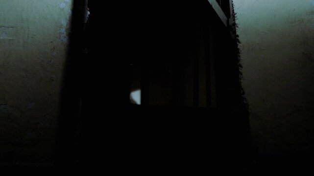 An authentic old prison cell, taken outside at ground level. the door is opening, showing the mighty shadow of the door bars onto the small cell, and a bit of a rug on the floor. a slow motion clip.