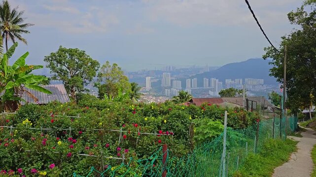 Panoramic view of Penang city and George Town from Penang Hill viewpoint. Urban landscape with high-rise buildings, mountains and tropical greenery under blue sky with clouds. Scenic overlook of islan