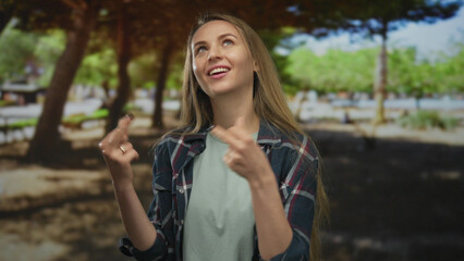 Naklejka premium Woman smiling with long hair gesturing outdoors in a green park with a plaid shirt in bright daylight