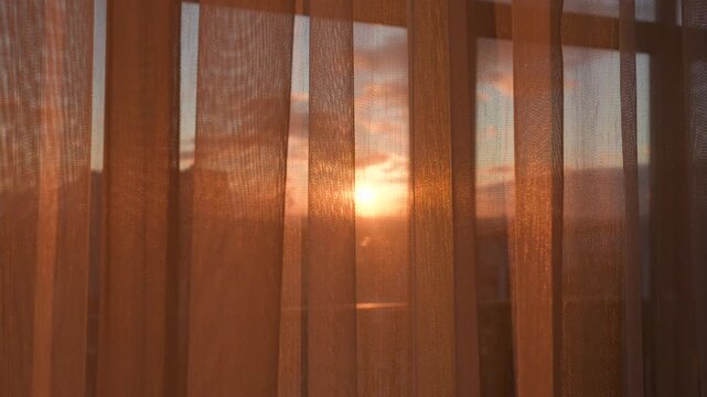 Beautiful morning sun shining through translucent curtains, creating warm and peaceful atmosphere in room while outside city is waking up in early morning light. Sunset shines through tulle
