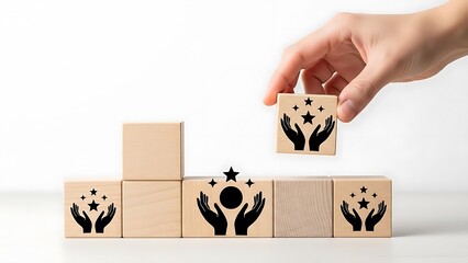 A hand placing a wooden block with a star and hands design on top of other blocks with similar designs on a white surface