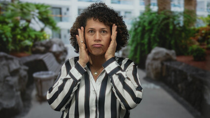 Middle aged hispanic woman clenches fists outside building wearing striped shirt; anxiety...