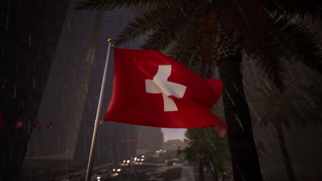 Switzerland national flag waving during winter rainfall above an alpine city with cold weather atmosphere.
