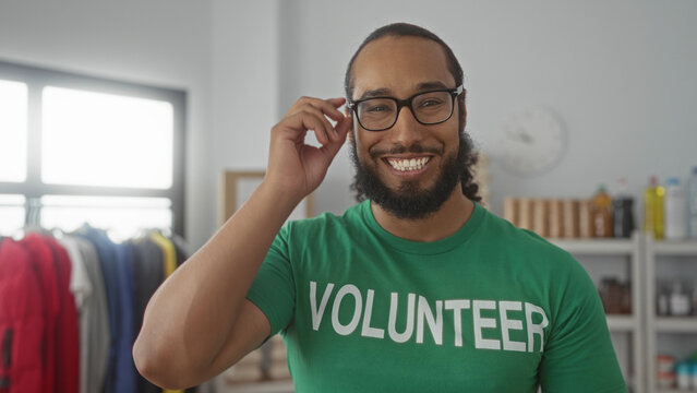 Man adjusts glasses while smiling in donation building with clothing rack and food shelves visible; generosity community service.