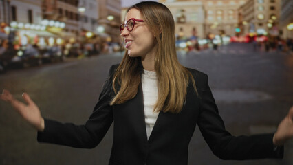 Woman placing hands over chest on cobblestone street at night, smiling with red glasses and black...