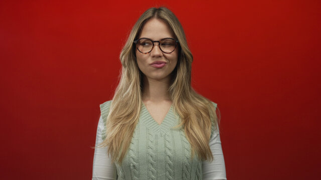 Young blonde caucasian woman holds hands together in a plotting gesture in a studio photo shoot; cunning mischief strategy.