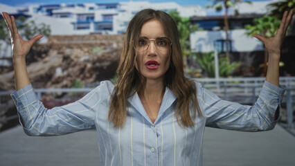 Woman gesturing with hands and raised palms on a street with visible building facades and boardwalk; animated conversation.
