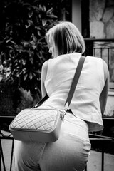 Black and white artistic shot of a woman in a white suit with a quilted crossbody bag, looking away.