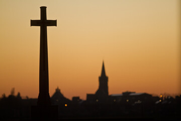 WWI Cross of Sacrifice overlooking a Flemish village at sunset. World War I military memorial with church steeple in the background. Flanders Fields Western Front remembrance Belgium.
