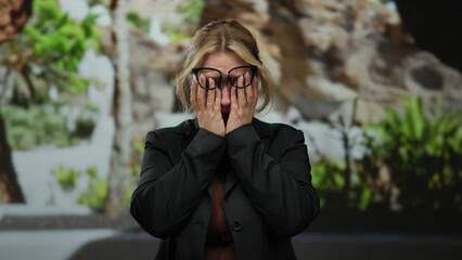 Young blonde woman crying with hands on face in an outdoor park setting, expressing emotion and...