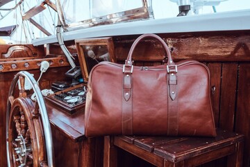Brown premium leather travel bag placed on a wooden deck of a luxury sailing yacht.