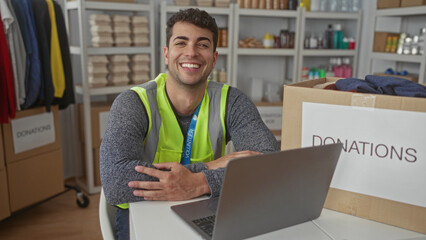 Man uses laptop while smiling inside center as hispanic volunteer and charity guy manages donations...