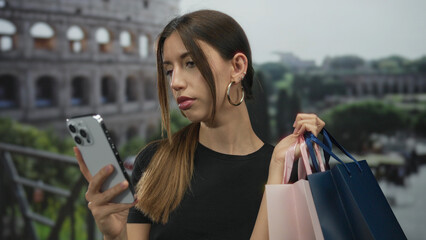 Young hispanic woman holds smartphone in one hand and blue and pink shopping bags at coliseum...