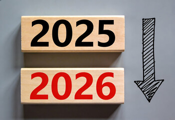 Decline concept of happy new year from 2025 to 2026 on wooden blocks with falling black arrow symbol over grey background