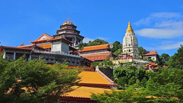 Kek Lok Si Buddhist temple complex on hillside in Penang, Malaysia. Colorful pagodas, shrines and white tower with golden spire surrounded by lush green trees. Traditional Asian architecture under blu