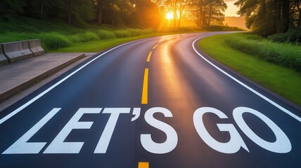 "LET'S GO" text painted on a curving road at sunset with trees and grass