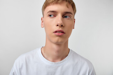 Young man with a calm thoughtful look wears a white tee against a neutral background, cropped to shoulders, conveying simplicity, focus and modern minimalism for fashion or lifestyle projects