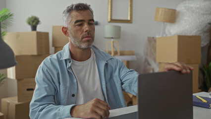Man holding smartphone at desk amid packed moving boxes in a residential building, tapping screen...