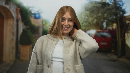 Fototapeta premium Woman smiling on a charming urban street wearing a cozy sweater, surrounded by quaint houses, trees, car, and showcasing youthful, cheerful energy.
