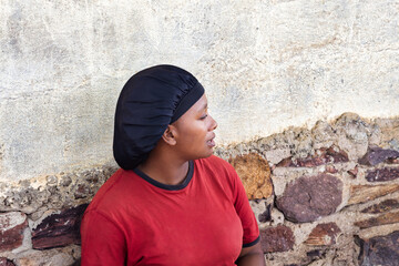 village african woman portrait, satin hair cap bonnet , outdoors in the nature, at home ,wall behind