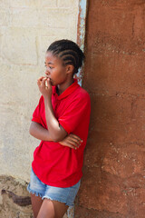 village african young girl teenager, with braids hairstyle , outdoors in the nature, at home , in front of the house wall